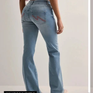 Ljusblå bootcut jeans  - Snygga ljusblå jeans med bootcut och rosa broderi på bakfickorna. Jeansen har klassisk femficksdesign och är tillverkade i mjukt denimtyg. Oanvända. Storlek 34. Säljer då de inte kommer till användning. Nypris 699kr.