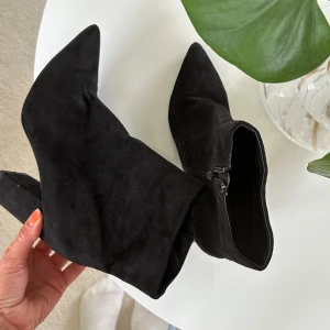 Svarta ” mocka ” stövletter med klack - Snygga svarta stövletter i mocka med spetsig tå och hög blockklack. Skorna har dragkedja på insidan för enkel påtagning och en stilren, minimalistisk look som passar till många outfits.