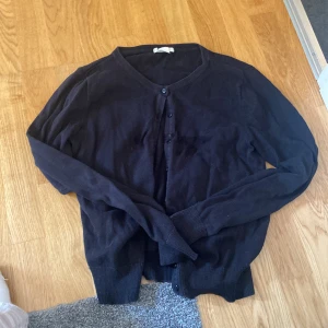 Svart kofta från H&M BASIC, storlek S - En svart, klassisk kofta från H&M BASIC i storlek S. Koftan har rund halsringning, långa ärmar och knäppning framtill med svarta knappar. Perfekt att slänga över en t-shirt eller linne. Mjuk och tunn, passar året runt.