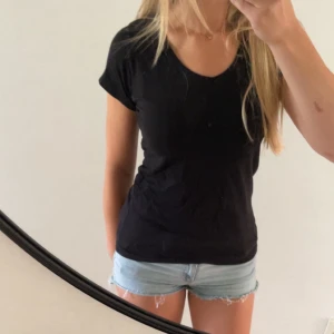 Svart basic t-shirt med v-ringning - Enkel svart t-shirt med v-ringad hals och korta ärmar. Sitter snyggt och har en klassisk passform som funkar till allt. Perfekt att matcha med jeans eller shorts för en clean look.