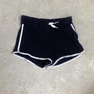 Svarta shorts med vit kant H&M - Svarta shorts från H&M i mjuk ekologisk bomull. De har vit kant längs benen och midjan, samt snörning framtill. Modellen är kort och har en sportig vibe, perfekt för sommardagar eller träning. Sitter midwaist och har en relaxed passform.