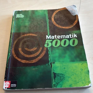 Matematik 5000 2b - Matematikbok för gymnasiet, kurs 2b, från serien Matematik 5000. Omslaget är grönt med abstrakta mönster i brunt och svart. Boken är på svenska och används ofta i svenska gymnasieskolor för matematikundervisning.