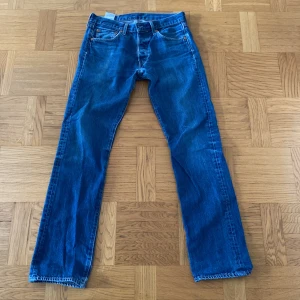 Levi's Premium blå jeans - Säljer ett par klassiska blå Levi's Premium jeans med raka ben och normal passform. Jeansen har fem fickor, knappar i gylfen och tydliga Levi's-detaljer som läderpatch och röd etikett bak. Perfekta för en stilren och tidlös look.