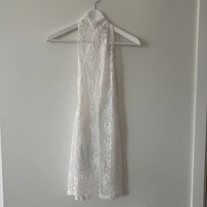 Vit spetsklänning från I.AM.GIA🤍 - Säljer en vit spetsklänning från I.AM.GIA med hög hals och knytning i nacken. Klänningen är ärmlös och har en figurnära passform med vacker spets över hela plagget. Perfekt för sommarens tillfällen🤍🤍