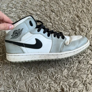 Nike Air Jordans Smoke Grey - Säljer ett par klassiska Nike Air Jordans med högt skaft i vitt och ljusgrått med svarta detaljer och svart swoosh. Skorna har svart snörning och perforerad tå för extra ventilation. Perfekta för dig som gillar streetwear och sneakers med ikonisk design. Originalpris 2500kr.