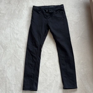 Svarta jeans från Tiger of Sweden - Säljer ett par svarta jeans från Tiger of Sweden. Byxorna har klassisk femficksdesign, raka ben och normal passform. Perfekta för dig som gillar stilrena och tidlösa plagg. Diskret logga på bakfickan och patch i midjan.