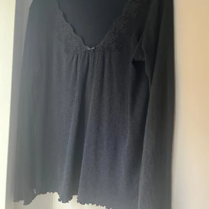 Svart långärmad topp med spets från Odd Molly - Supersöt svart långärmad topp från Odd Molly med ribbad struktur, spetsdetaljer vid ringningen och en liten rosett framtill.