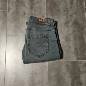 Grå jeans från dondup Model George - Säljer ett par grå jeans från dondup George med klassisk femficksdesign och raka ben. Byxorna har en enkel stil med orange detalj på bakfickan och passar perfekt till vardags. Midjan är normal och materialet känns slitstarkt.
