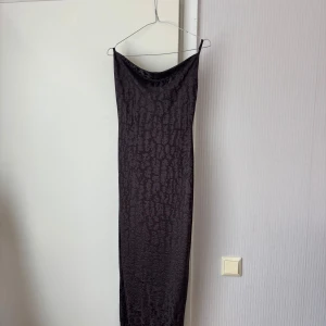 Mörkgrå långklänning med mönster  - Säljer en mörkgrå långklänning från NA-KD med diskret mönster och smala axelband. Klänningen har en draperad urringning och figurnära passform, med öppen rygg. Endast använd en gång. Jag bär vanligtvis storlek S/M. Tveka inte på att höra av dig vid frågor eller prisförslag!