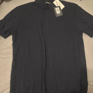 Mörkblå pikétröja från Dressmann - Snygg mörkblå pikétröja från Dressmann med klassisk krage och knappar framtill. Perfekt för en stilren och avslappnad look. Tillverkad i mjuk bomull för extra komfort.