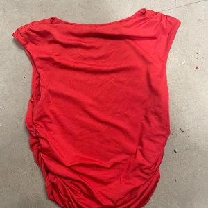 Röd topp med rynkade sidor från SHEIN - Säljer en röd topp från SHEIN i storlek S. Toppen har rynkade detaljer längs sidorna och är tillverkad i ett mjukt, stretchigt material. Perfekt för dig som gillar en enkel men snygg look.