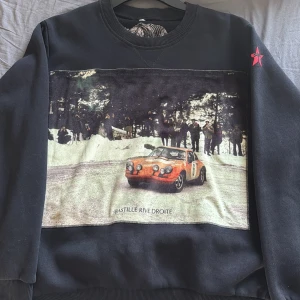 Svart Bastille Rive Droite tröja - Svart sweatshirt med stort tryck på bröstet. Rund halsringning med röd bastille täcken på axeln.