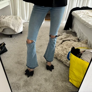 Ljusblå bootcut jeans med slitningar - Säljer ett par ljusblå bootcut jeans med slitna detaljer vid knäna och råa kanter. Jeansen har hög midja och klassisk femficksdesign. Perfekta för en avslappnad och trendig look. Super snygga!🥰