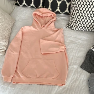 Aprikos färgad  hoodie från Cubus - Mysig aprikos hoodie från Cubus med klassisk känguruficka och huva. Tröjan är tillverkad i en mjuk bomulls- och polyestermix och har långa ärmar samt ribbade muddar vid ärmslut och nederkant.