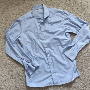 Ljusblå skjorta från Eton - Säljer en klassisk ljusblå skjorta från Eton i slim fit. Skjortan har lång ärm, knappar framtill och diskret mönster i tyget. Perfekt för dig som gillar stilrena och snygga skjortor.