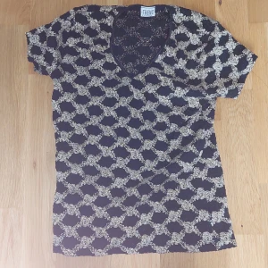 Svart och guld mönstrad t-shirt från Trend report - Kortärmad t-shirt från Trend report i svart med guld mönster och v-ringning. Perfekt för dig som gillar unika mönster och vill ha en bekväm topp med snygg passform.