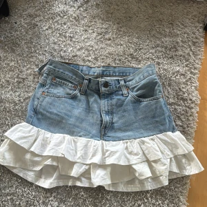 Jeanskjol med volang från Levi's - Supersöt jeanskjol från Levi's med bred vit volangkant nedtill. Kjolen är gjord av ett par gamla Levis jeans och volangen är påsydd av mig. Det finns ingen storlek i den men måttet tvärs över midjan är 38 cm och längden på hela kjolen är 35 cm