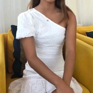 Vit one shoulder klänning med volang - Superfin vit klänning med one shoulder och puffärm. Klänningen har broderade hål och volang nertill, vilket ger en romantisk känsla. Den är från bershka men den gamla ägaren har klippt av märket ❤️