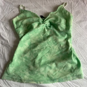 Ljusgrön linnetopp med smala axelband - Säljer en ljusgrön linnetopp med blommor. Den har smala axelband och lätt twistad detalj framtill. Toppen har en mjuk, figurnära passform och är perfekt för varma dagar. Materialet känns svalt och bekvämt mot huden. Storleken är M men passar till S