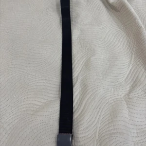 Svart tygbälte med metallspänne - Säljer ett svart bälte i tyg med ett stilrent, matt metallspänne. Bältet är enkelt att justera och passar till många olika outfits. Perfekt för dig som vill ha en clean och modern look.