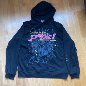 Svart hoodie SP5DER med tryck och huva - Svart hoodie från SP5R i 100% bomull med stor färgglad spindelnätsgrafik och texten 'prank!' på bröstet. Hoodien har huva, långa ärmar och ribbade muddar. Perfekt för dig som gillar streetwear och coola prints.