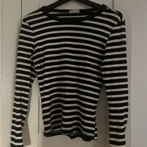 Svartvit randig långärmad tröja - Säljer en svartvit randig långärmad tröja med klassisk rund hals. Tröjan har smala horisontella ränder och är i ett mjukt, stretchigt material som sitter snyggt på kroppen. Perfekt för dig som gillar en enkel men stilren look.