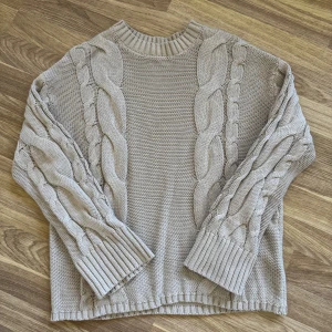 Beige stickad tröja från Lager 157  - Säljer en beige stickad tröja från 157 i storlek XS. Tröjan har grova flätstickade detaljer längs ärmar och fram/baksida, samt ribbade muddar och halsringning. Perfekt för lager-på-lager och chill höst/vinterstil. Knappt använd 
