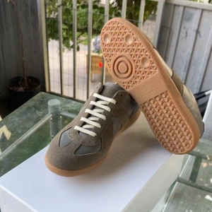Maison Margiela GATS - Maison Margiela sneakers i grått och grönt i mocka och skinn. Klassisk retrodesign med vita snören och gummisula. Skorna är använda ett fåtal gånger. Anledningen till att jag säljer skorna är att dem sitter för smått för mig.