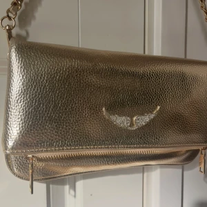 Zadig & Voltaire väska - Säljer en guldig väska från Zadig & Voltaire med en kortare och en längre kedja. Väskan har dragkedja och magnetlås. Perfekt för dig som vill sticka ut med en lyxig vibe. Väskan är i super bra skick. Säljer eftersom jag slutat använda den ❤️