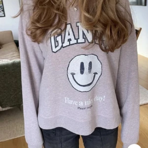 Ljusgrå ganni tröja med smiley - Supermjuk ljusgrå tröja från Ganni med stort smiley-tryck och texten 'Have a nice day!' framtill. Långärmad och i avslappnad passform, perfekt till jeans. Tillverkad i bomullsmix för en skön känsla. Storlek xs/xxs men passar S