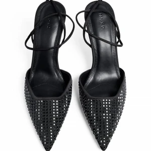 Svarta pumps med spetsig tå från NA-KD - Snygga svarta pumps från NA-KD med spetsig tå och hög klack. Skorna har ett coolt rutigt mönster framtill och tunna remmar som knyts runt vristen. Tillverkade i syntetmaterial med elegant finish, perfekta för att lyfta din outfit.