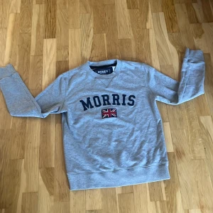 Grå sweatshirt från Morris XS-S - Säljer en grå sweatshirt från Morris i storlek XS men passar också bra på S. Tröjan har rund hals, långa ärmar och tryckt Morris-logga med brittisk flagga framtill. Perfekt för en chill och stilren look. Materialet är mjukt och skönt, troligtvis bomull eller bomullsblandning. Tröjan är väldigt bra skick.