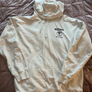 Vit hoodie från Moschino med tryck - Moschino Milano Hoodie – Vit – Storlek L  Säljer denna stilrena och exklusiva hoodie från Moschino i klassisk vit färg. Tryck både fram och bak med det ikoniska Moschino Milano-logot. Perfekt för dig som vill sticka ut med en designerlook, samtidigt som du håller det avslappnat och bekvämt.  🔹 Färg: Vit 🔹 Storlek: L 🔹 Passform: Normal fit 🔹 Material: Bomull 🔹 Skick: mycket bra  🔹 Detaljer: 	•	Stor logga med tryck på ryggen 	•	Mindre logga på bröstet Skriv för frågor!
