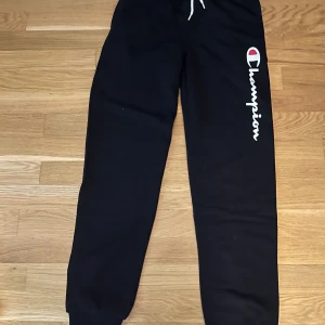 Svarta Champion och grå Adidas mjukisbyxor - Två par mjukisbyxor: ett par svarta från Champion med vit snörning och logga längs benet, samt ett par ljusgrå från Adidas med stor svart logga på låret. Båda har resår i midjan och är perfekta för chill eller träning. Adidas byxorna är från 13/14 år ( 164 cm ). Champion byxorna är också 13/14 år mellan (162&167) 50 kr styck. 90kr för båda 