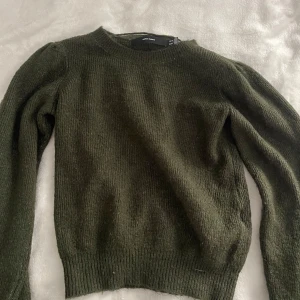 Mörkgrön stickad tröja Vero Moda - Mysig mörkgrön stickad tröja från Vero Moda med rund halsringning och långa ärmar. Tröjan har en enkel, klassisk design med ribbade muddar vid ärmslut och nederkant. Perfekt för lager-på-lager och chill höst- och vinterstil.