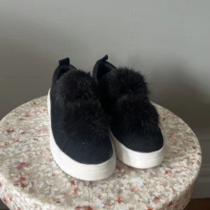 skor med fluff - Unika svarta sneakers från Timberland med fluffig pälsdetalj på ovansidan och vit platt sula. Skorna är i mocka och har en cool slip-on design som sticker ut. Perfekta för dig som vill ha något extra till din outfit. köpta från duffy! den har en liten vit fläck från nagellim därför priset 