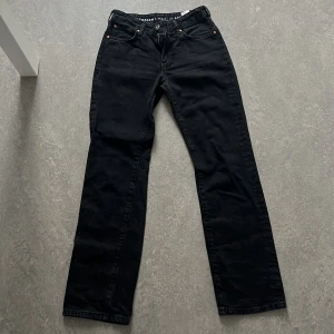 Svarta low straight jeans W24 L32 - Snygga svarta jeans med low waist och raka ben. Klassisk femficksmodell med silverfärgade nitar och knapp. Jeansen har en stilren look och passar perfekt till sneakers eller boots. Materialet är jeans och modellen är straight fit.