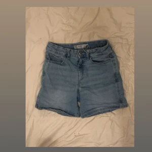 Ljusblå jeansshorts från Cubus - Snygga ljusblå jeansshorts från Cubus med klassisk femficksdesign och knappgylf. Perfekta för varma dagar och enkla att matcha med allt. Shortsen har en normal passform och är tillverkade i mjukt jeanstyg för extra komfort.