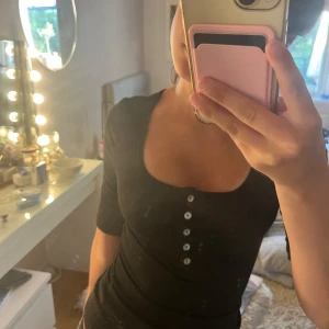 Svart ribbad topp med knappar H&M XS - Svart ribbad topp från H&M i storlek XS. Modellen har en djup rundad ringning, korta ärmar och vita knappar framtill. Toppens material är mjukt och stretchigt aldrig använt💞💞