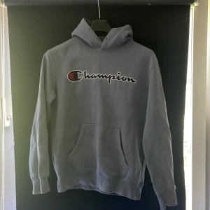 Ljusblå Champion hoodie med logga - Säljer en ljusblå hoodie från Champion i storlek S. Tröjan har stor broderad Champion-logga på bröstet, känguruficka och huva. Perfekt för chill dagar och streetwear-stil. Mjuk insida och klassisk passform. 