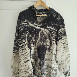 Svartvit skjorta Eytys Otis Zorn - Unik svartvit skjorta från Eytys med konstnärligt tryck inspirerat av etsningar av Anders Zorn. Skjortan har lång ärm, klassisk krage och knappar framtill. Oversized fit och tillverkad i ett mjukt, glansigt material som känns lyxigt mot huden. Ord pris 4000 kr.