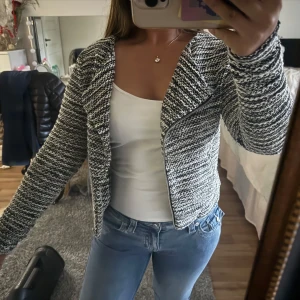 Svartvit stickad cardigan jacka - Säljer en svartvit stickad cardigan jacka med dragkedja framtill. Jackan har ett coolt randigt mönster och är långärmad med en lite bredare krage. 