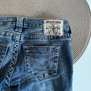 True Religion blå bootcut jeans - Säljer dessa supersnygga lågmidjade jeans ifrån true religon! De är något slitna längst ner där bak men inget man tänker på. Säljes då de ej kommer till användning 💕                                            Midjemått: 35 cm rakt över                Innerbenslängd: 80 cm                   