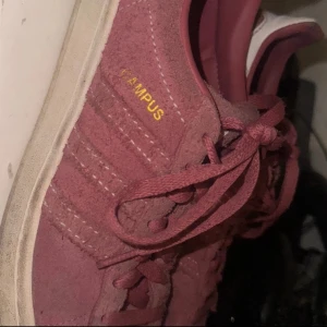 Adidas Campus sneakers i vinröd mocka - Säljer ett par Adidas Campus sneakers i vinröd mocka med klassiska tre ränder på sidan och gul CAMPUS-text. Skorna har snörning, vit detalj vid hälen och platt sula. Perfekta för dig som gillar retrovibbar och snygg streetstyle.