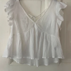 Vit v-ringad blus med volangärmar - Supersöt vit blus i luftig bomull med omlott-look och v-ringning både fram och bak. Blusen är från Nelly och aldrig använd då den inte riktigt är min stil, den har även lapp kvar lapp kvar.💗strlk 36