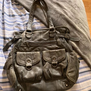 Mörkgrön skinnväska från InWear med fickor - Rymlig mörkgrön axelväska i skinn från InWear med två stora framfickor med lock och ringdetaljer, dragkedja upptill och justerbara sidoremmar. Invändigt finns flera fack för småprylar. Perfekt för dig som vill ha plats för allt och ändå se stilren ut. Får plats med skoldator och är perfekt för en stor packning, för kanske en sleepover?😸💕 Lite små defekter på undersida och remmarna men inget märkbart!