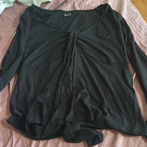 Svart omlottopp från Gina Tricot XL - Svart långärmad topp från Gina Tricot i omlottmodell med snygg knytning framtill. Tunn och mjuk i materialet, perfekt för lager-på-lager. Djup v-ringning och smickrande passform. Storlek XL.
