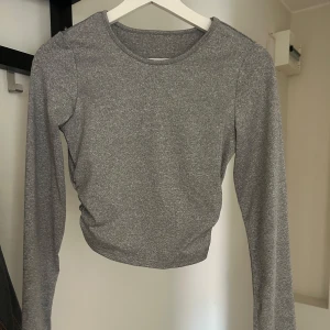 Grå långärmad croppad tröja - En stilren grå långärmad tröja med croppad passform. Tröjan har rund halsringning och är tillverkad i ett mjukt, stretchigt material som sitter snyggt på kroppen. Perfekt för dig som gillar en enkel men trendig look.