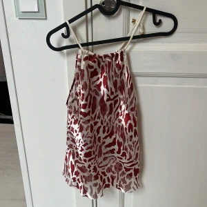 Röd och vit mönstrad linnetopp Elen Shando - Säljer en snygg linnetopp från Elen Shando med röd och vit camouflageinspirerad print. Toppen har tunna axelband och är tillverkad i ett glansigt, lätt material som känns luftigt och fräscht. Saknar prislapp men skulle uppskatta att den är s/m! 