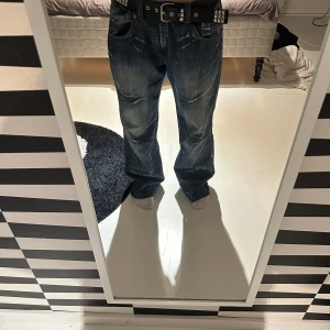 Blå baggy jeans med broderi - Säljer ett par mörkblå baggy jeans med bred passform och snygga broderade detaljer på bakfickorna. Jeansen har slitningar och coola kontrastsömmar, samt klassisk femficksdesign. Perfekta för dig som gillar streetstyle och vill sticka ut.